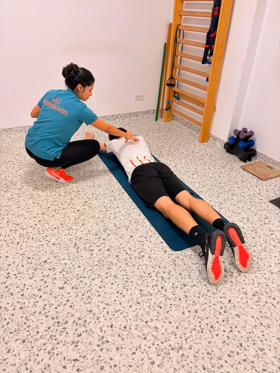 Kinetoterapeut care ghidează un pacient într-un exercițiu de întindere, cu pacientul poziționat culcat pe burtă