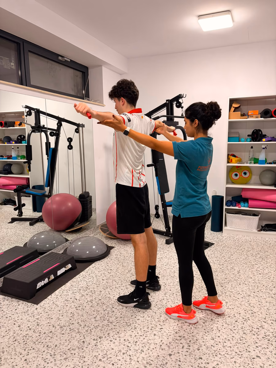 Kinetoterapeut care corectează postura brațului unui pacient în timpul unui exercițiu cu bandă elastică