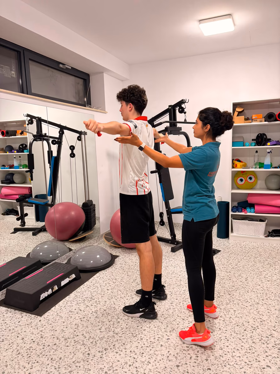 Vedere mai apropiată a aceluiași exercițiu cu bandă elastică, kinetoterapeutul ajustând poziția brațului pacientului